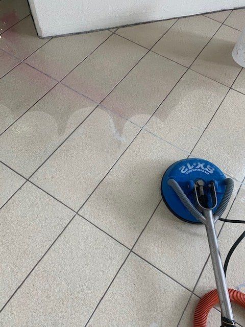 A Blue Vacuum Cleaner is Sitting on a Tiled Floor — The Tile & Stone Specialists in Peregian Beach, QLD