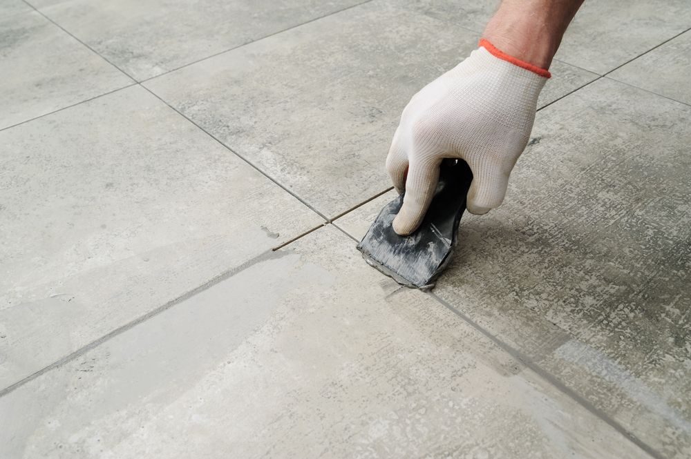 A Person is Applying Grout to a Tiled Floor With a Spatula — The Tile & Stone Specialists in Maroochydore, QLD