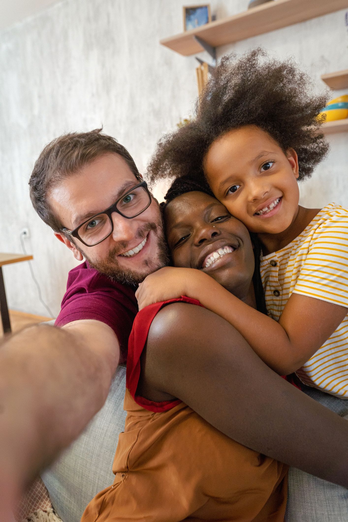 A man and woman are hugging a little girl while taking a selfie on a couch.