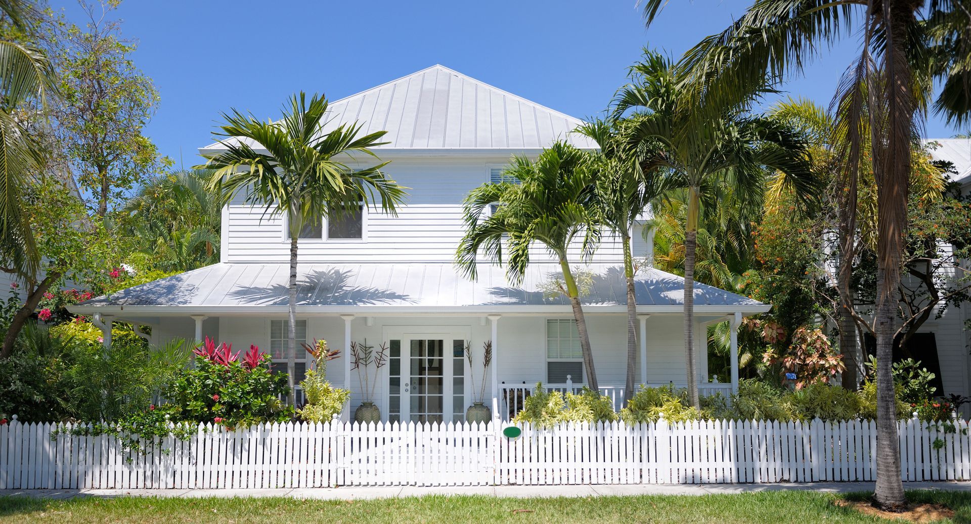 A white house with a white picket fence and palm trees in front of it