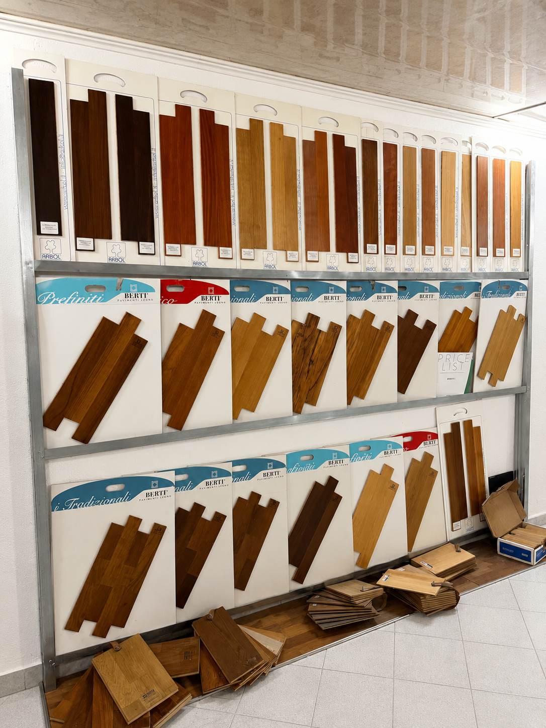 Campioni di legno disposti su scaffali a parete in uno showroom, con tavole sfuse impilate sul pavimento.