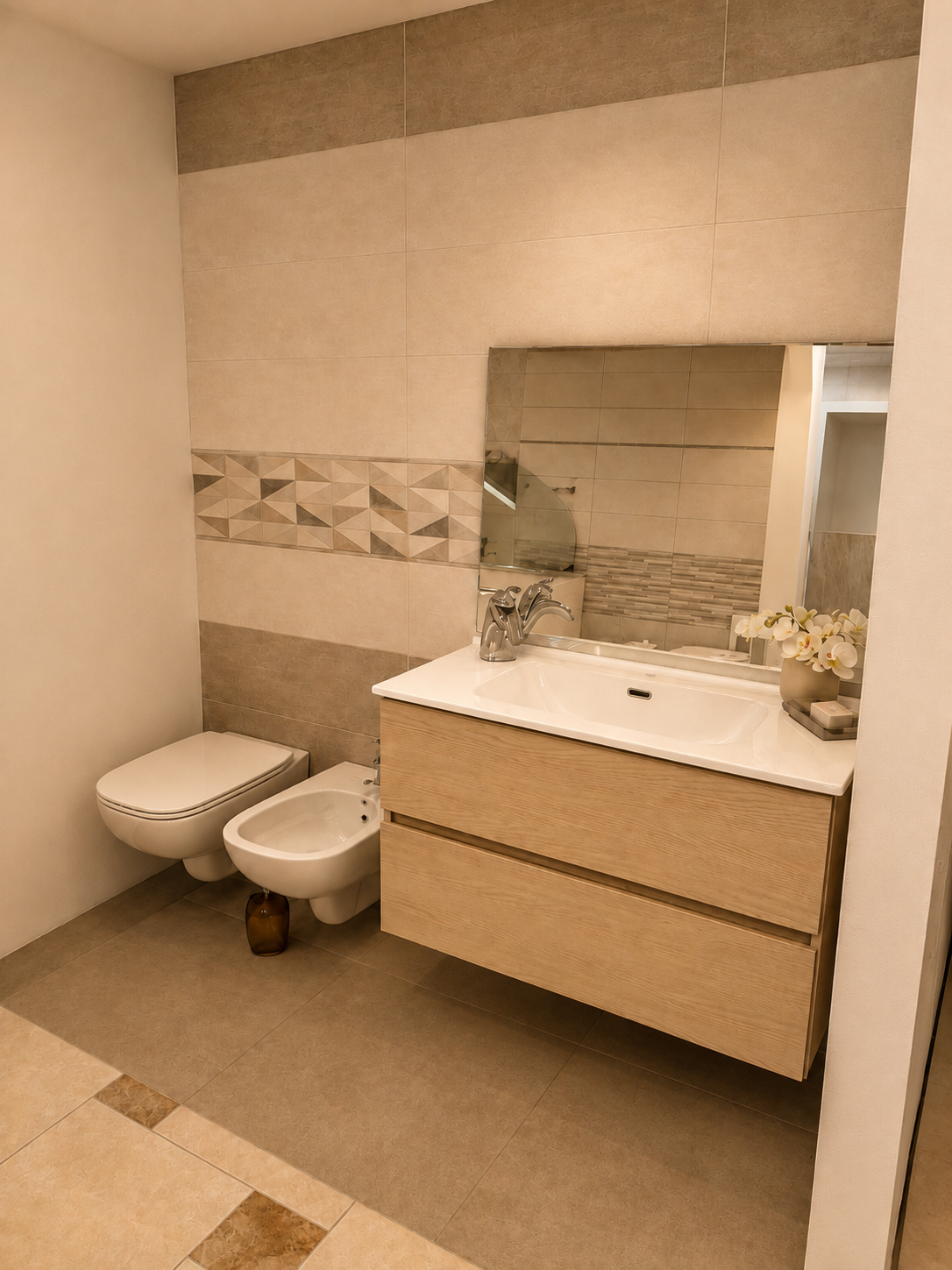 Piccolo bagno beige con WC, bidet e moderno mobile lavabo di fronte a uno specchio.