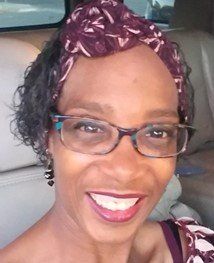 Woman with glasses and burgundy head wrap smiles.