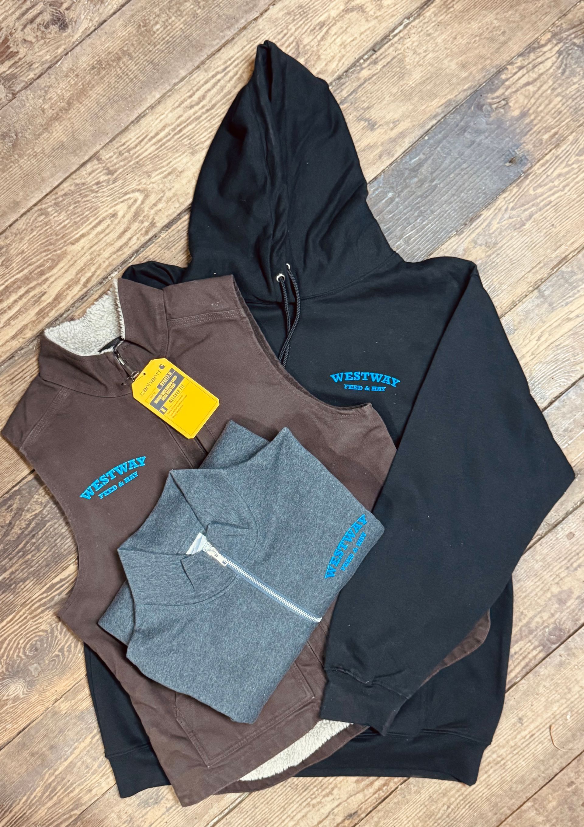 Stack of hoodies and long-sleeve shirts in black, brown, gray, and navy on a wooden floor