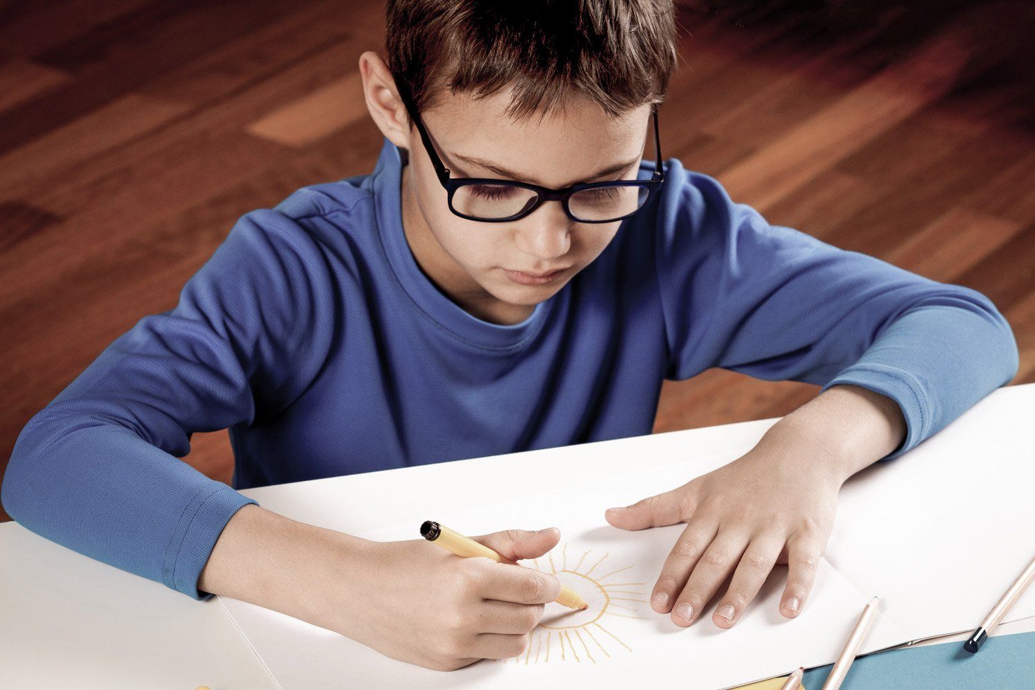 Ein kleiner Junge mit Brille schreibt auf ein Stück Papier