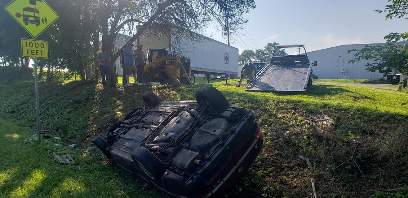 Overturned black car in a ditch near a road with a school bus warning sign.