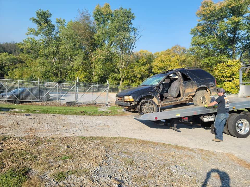 A damaged black SUV on a tow truck, being loaded by a person.