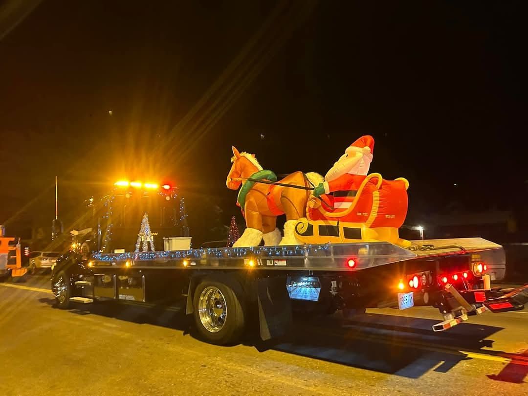 Santa and his sleigh statue on a flatbed tow truck at night, illuminated by emergency lights.