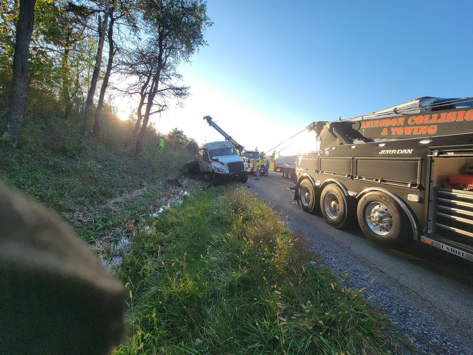 Tow truck pulling a semi-truck out of a ditch on a gravel road; sunny day.