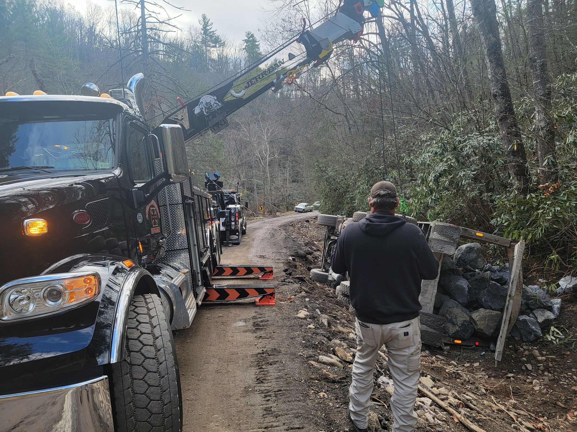 Tow truck on muddy road with a person filming. Forest background.