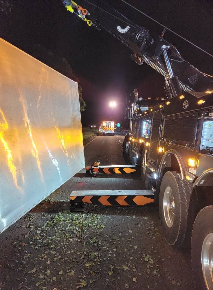 Tow truck hauling large white object on a dark road, illuminated by headlights.