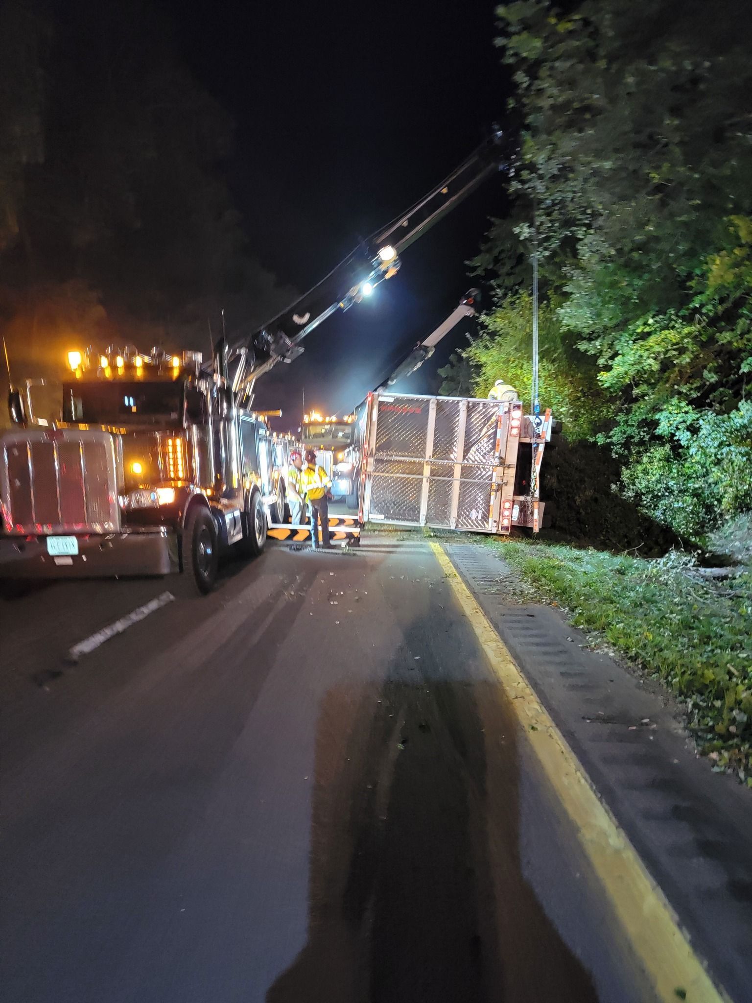A semi-truck on its side being righted at night with tow trucks, emergency workers, and street lights.