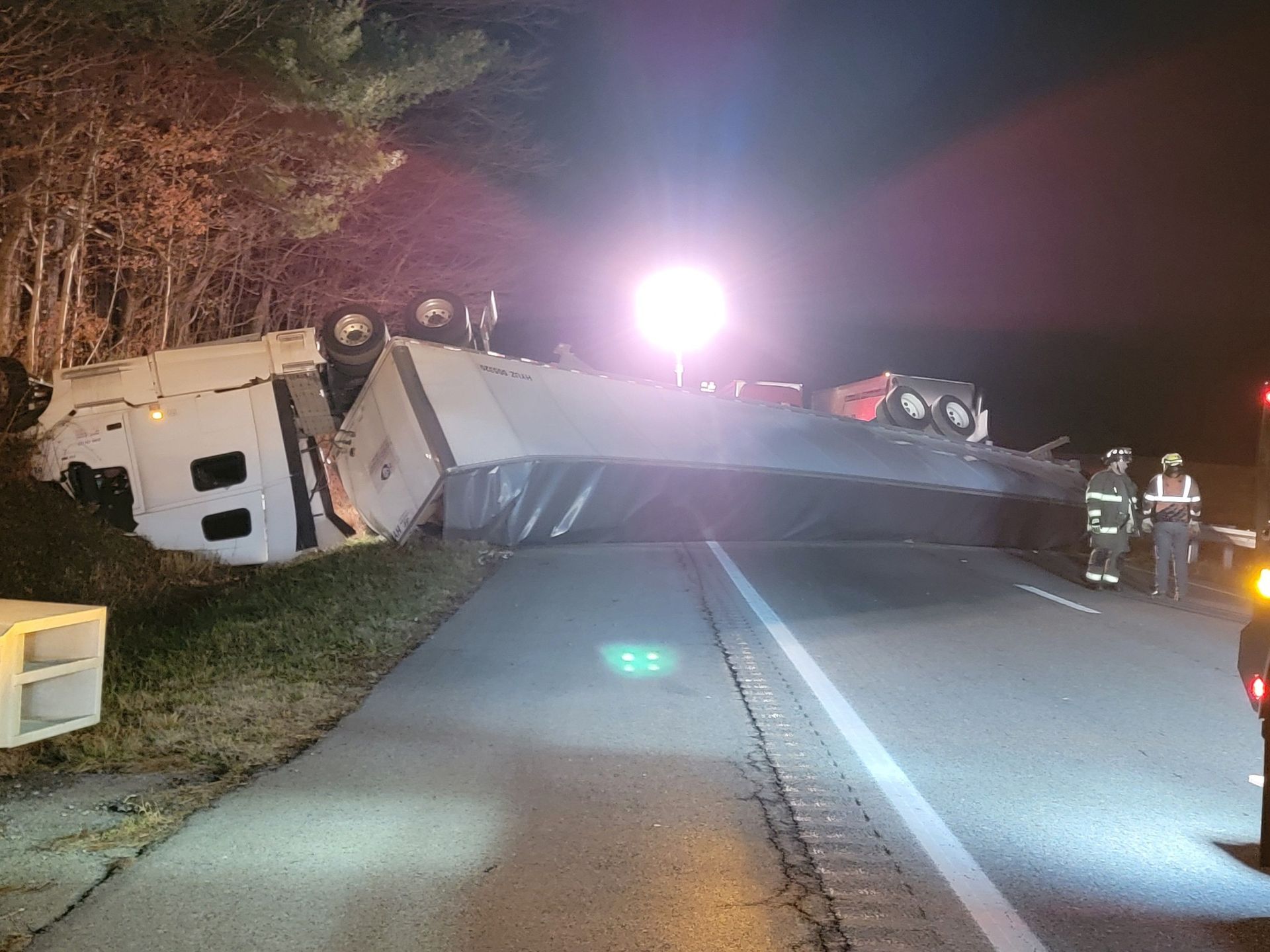 Overturned truck on road at night, emergency responders present.
