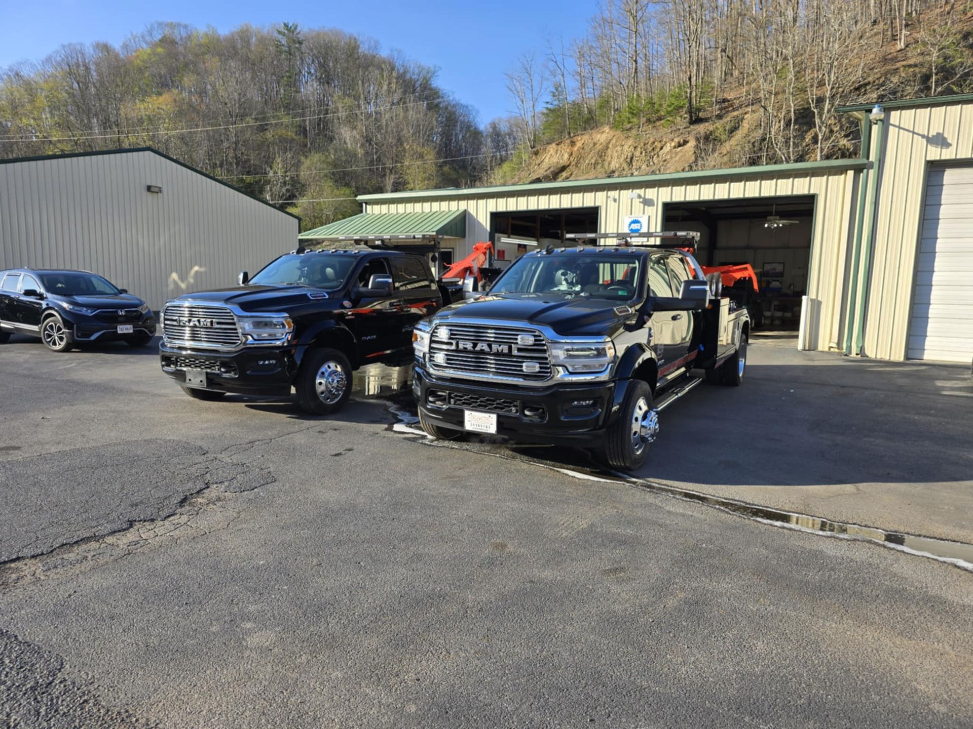 Two black pickup trucks parked in front of a building with garage doors. Paved area. Bright outdoor setting.