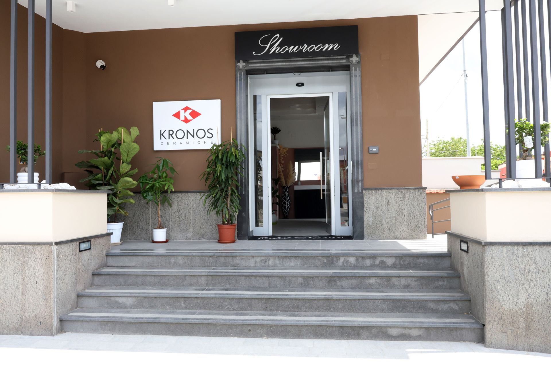 Ingresso principale con scalini, porte a vetri e insegna Kronos su un edificio beige.