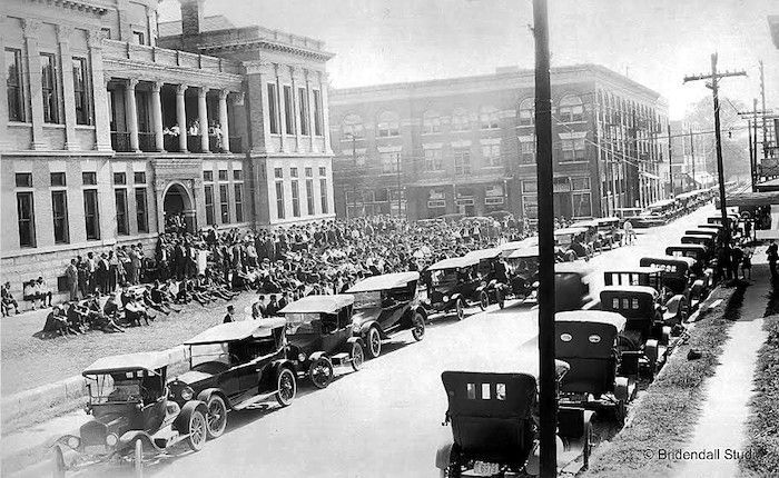 A black and white photo of cars parked in front of a building