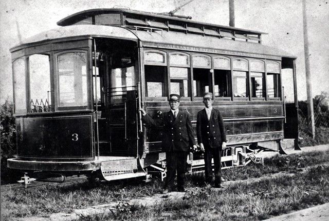 Two men are standing in front of a trolley with the number 3 on it