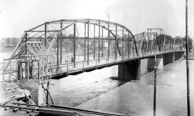 A black and white photo of a bridge over a river.