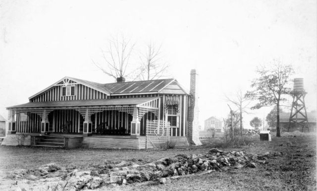 A black and white photo of a house with a water tower in the background.