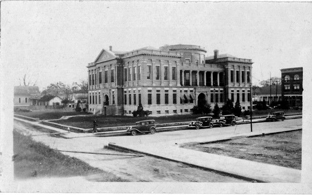 A black and white photo of a large building with cars parked in front of it