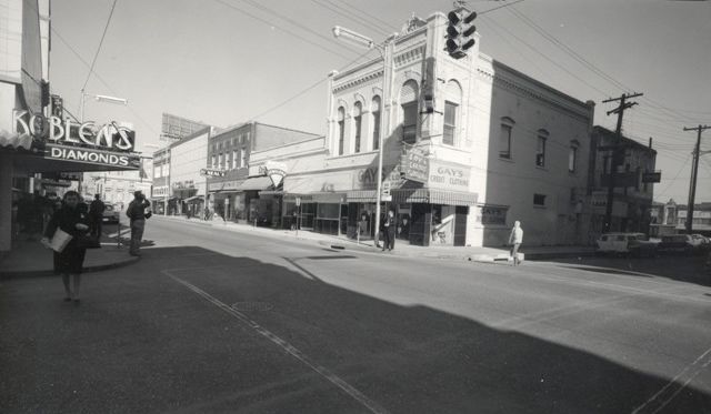 A black and white photo of a city street with a building that says ' noble 's diamonds ' on it.