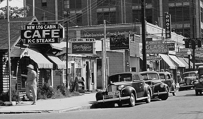A black and white photo of a city street with a sign that says cafe kc steaks
