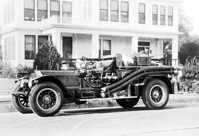A black and white photo of an old fire truck parked in front of a house.