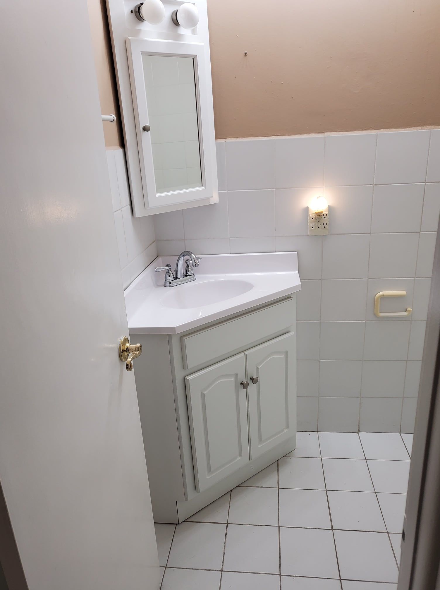 Small white bathroom with corner sink, mirror cabinet, tiled walls, and wall light.