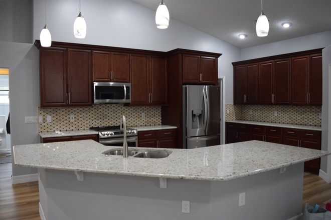 Modern kitchen with dark wood cabinets, stainless appliances, and a large light granite island.
