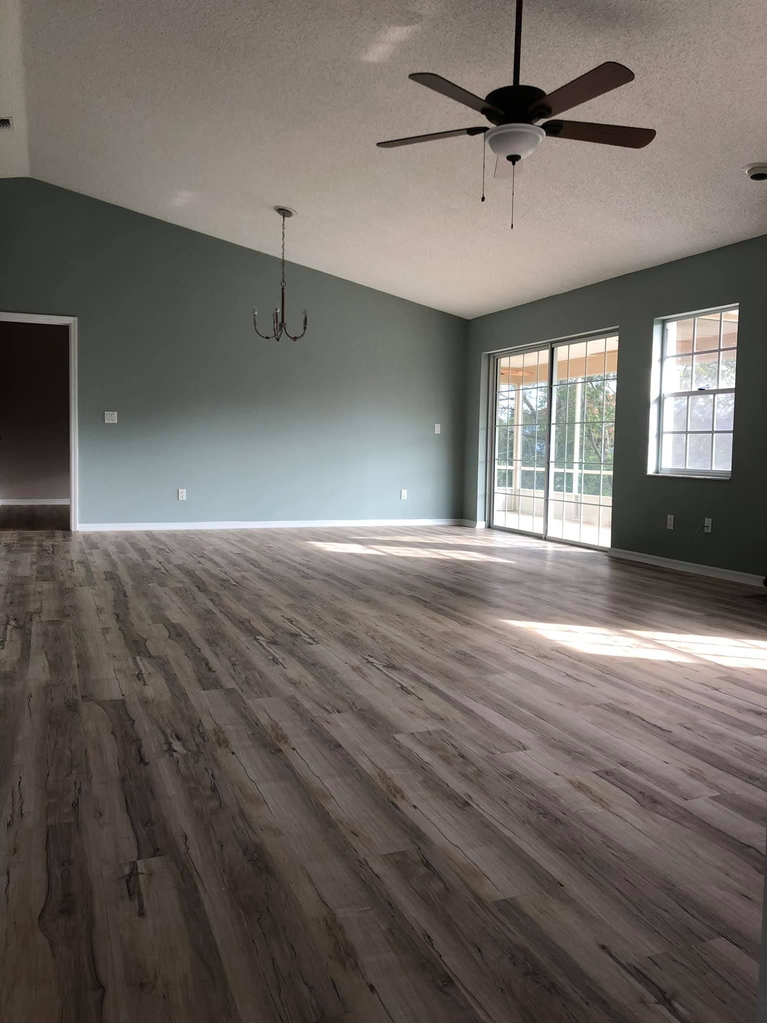 Empty living room with gray walls, wood-look floors, ceiling fan, and sliding glass doors letting in sunlight