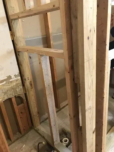 Framed wall studs and exposed plumbing inside an unfinished interior wall.