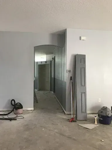 Unfinished interior hallway with gray walls, debris on the floor, and a door leaning against the wall.