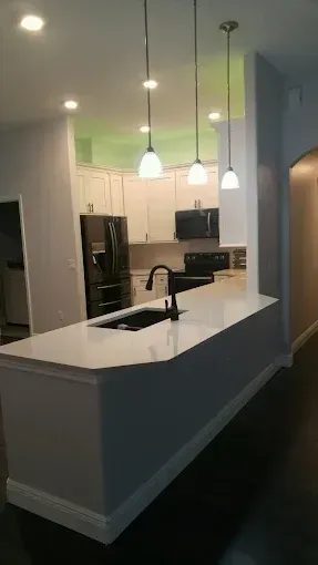 Modern kitchen with white cabinets, black island countertop, pendant lights, and a stainless-steel refrigerator
