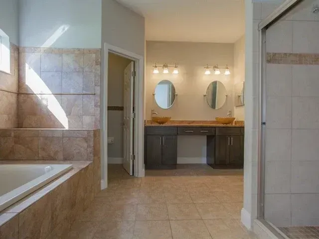 Bathroom with tiled walls, bathtub, double sink vanity, and mirrors under warm lighting