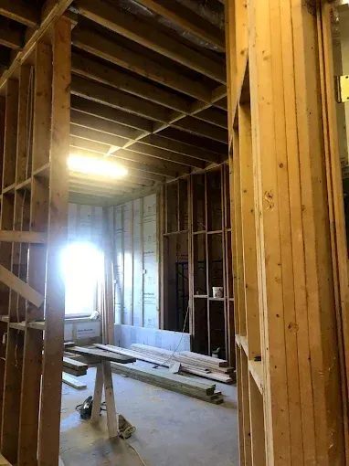 Partially renovated interior with exposed wooden framing, ceiling joists, and a bright window in back