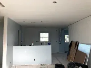 Empty room with unfinished white walls, a half wall, and construction materials leaning on the right side.