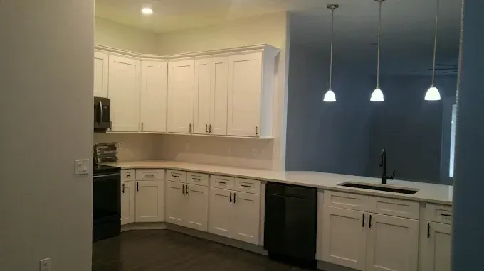 Bright, empty kitchen with white cabinets, dark countertops, and three pendant lights over a breakfast bar.