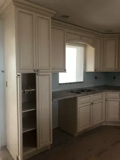 Empty kitchen with white cabinets, gray countertops, a window over the sink, and an open pantry cabinet.