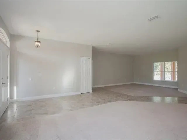 Empty living room with beige carpet, gray walls, and a window letting in daylight