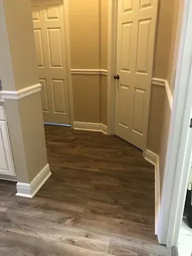 Narrow hallway with beige walls, white trim, closed doors, and dark wood flooring