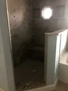 Dim shower stall with dark tile, a small octagonal window, and a white sink or tub edge in the foreground