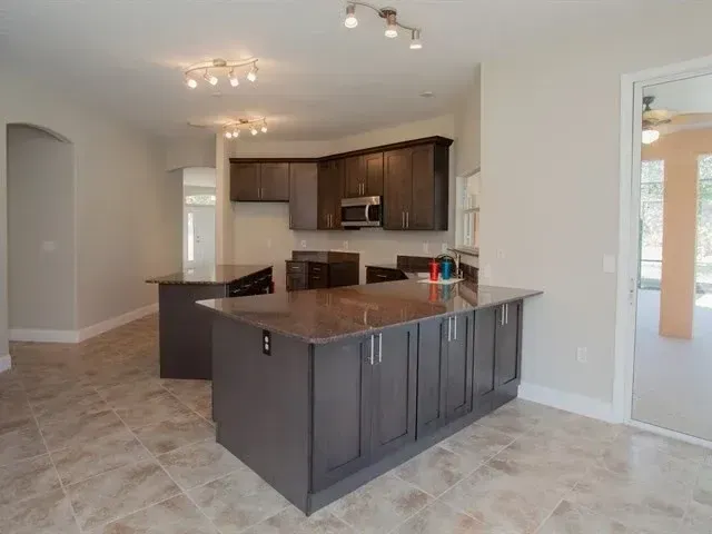 Empty modern kitchen with dark cabinets, island, and light tile flooring in a bright open room