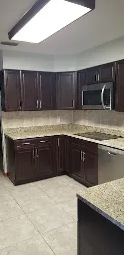 Modern kitchen with dark wood cabinets, beige countertops, tile floor, and stainless steel appliances