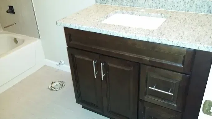 Bathroom vanity with dark wood cabinets, white countertop, and sink beside a bathtub.