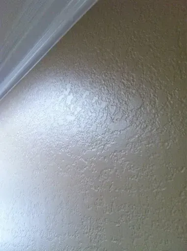 Textured beige wall with bright light reflecting near the ceiling corner