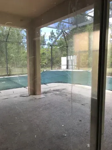 Empty screened-in pool area with turquoise water, concrete deck, and cracked floor.