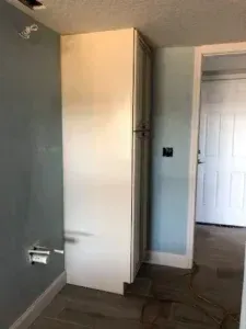 Empty room with a tall white cabinet, light gray walls, and a doorway to a hallway.