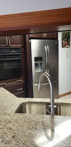 Modern kitchen with granite island, stainless steel refrigerator, and sink faucet in foreground