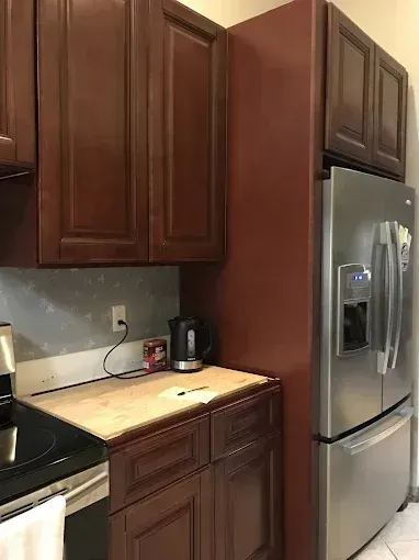 Kitchen counter with dark wood cabinets, beige countertop, and stainless steel refrigerator