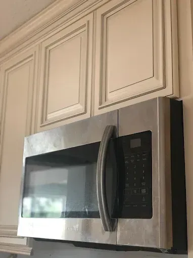 Stainless steel microwave mounted under cream kitchen cabinets, with black control panel and handle.